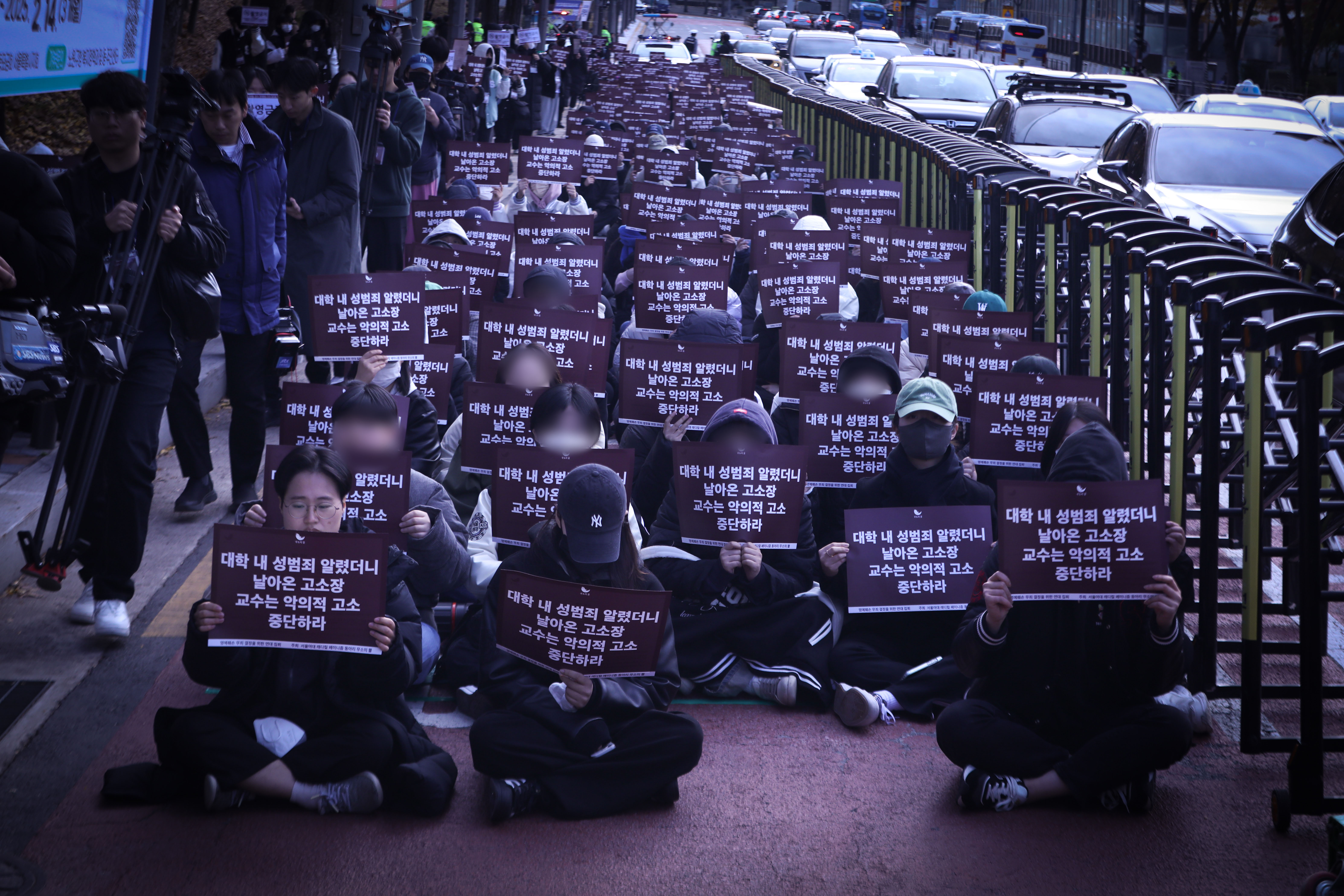 首爾女子大學學生在車來車往的警局前人行道席地而坐抗議，引起路過民眾關注。　圖／犀牛角（무소의 뿔）提供