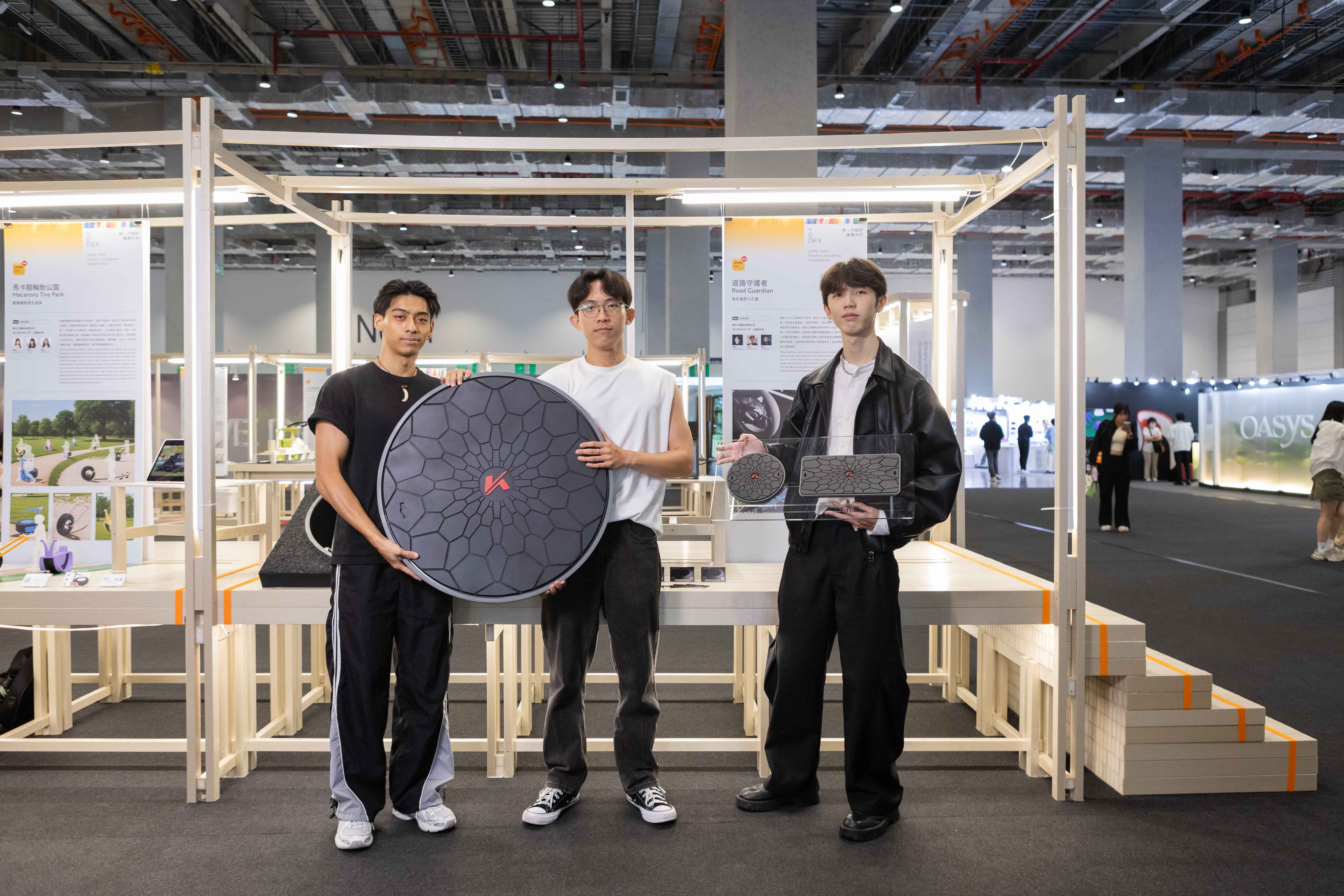 設計學生在展場，與再生橡膠人孔蓋模型合照，後方有設計細節介紹看板，說明理念與細節。　圖／設計團隊提供