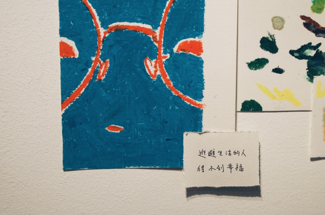 蔡汶澄在牆上貼上「逃避生活的人得不到幸福」的宣言，搭配一旁近距離的藍色大臉，帶來直面生活的壓迫感。　 圖／吳欣嬡攝